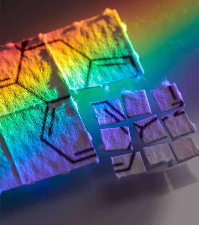 Mehrfarbige Papierquadrate, mit schwarzen Mustern, unter einem Regenbogen-Lichteffekt.